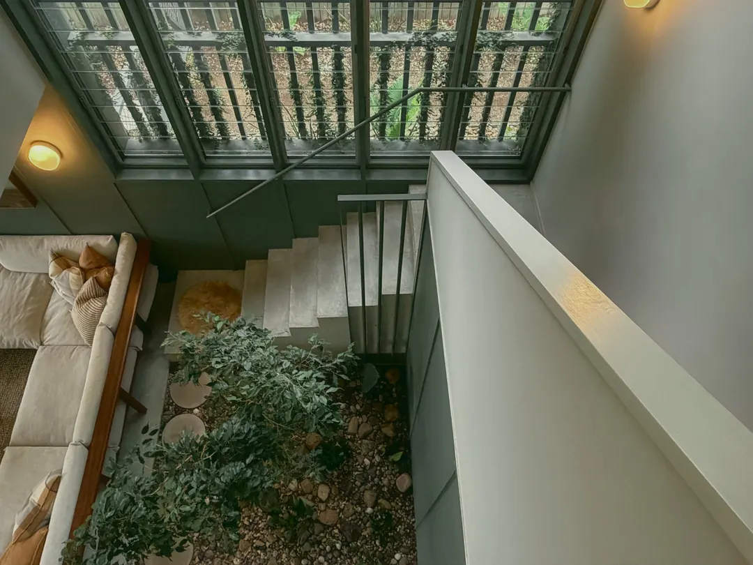 Looking down from the upstairs windows to the stairs, the lounge and the fig growing among river stones in the indoor garden