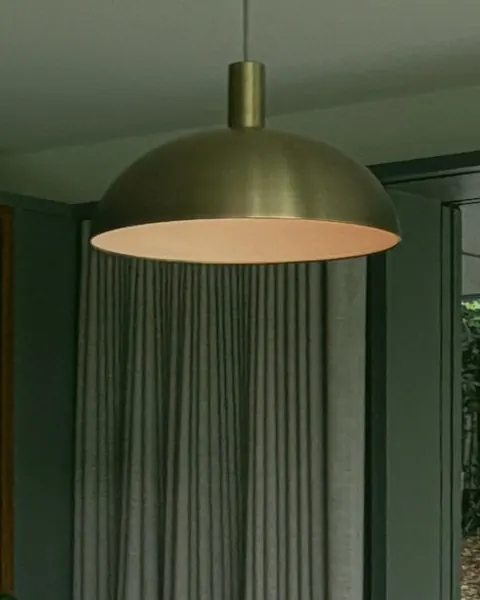 A brass dome pendant light hanging in front of a linen curtain