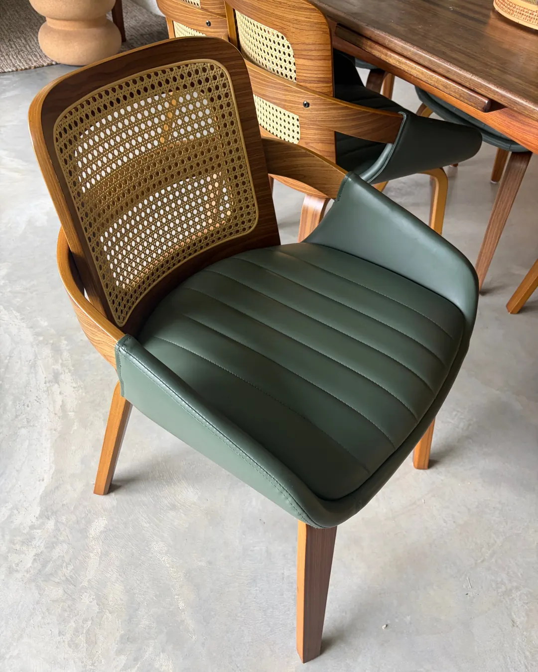 A walnut dining chair with a woven cane back and a channel-stitched green seat, beside the dining table