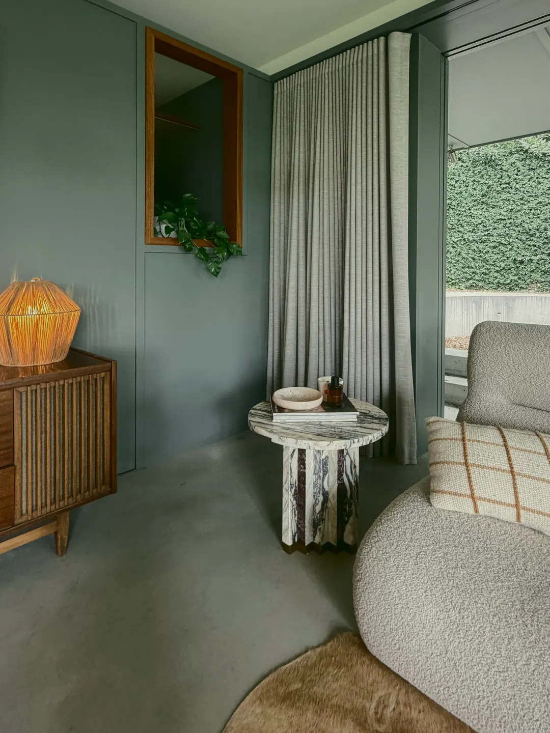 A rattan lamp on a timber radiogram beside a marble side table and a linen curtain