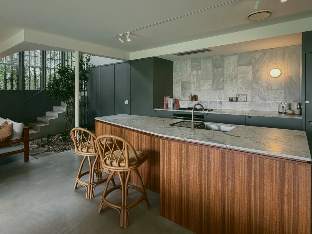 Kitchen island clad in spotted gum, with rattan counter stools and a marble top