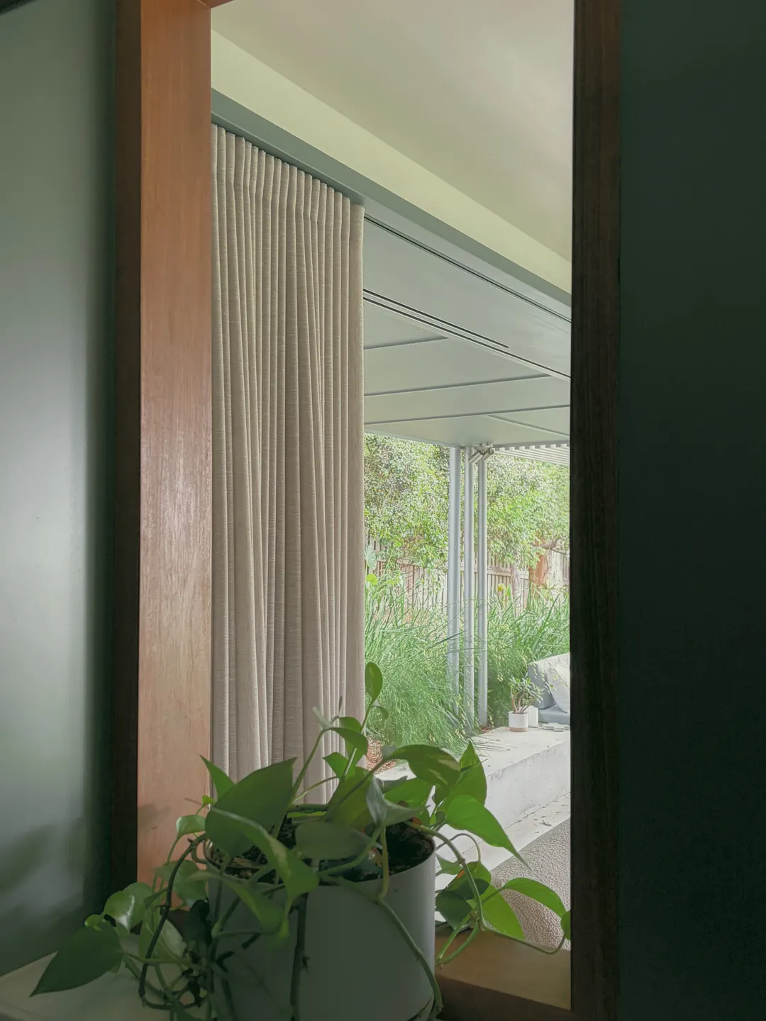 A timber frame and linen curtain with a pothos, the garden beyond