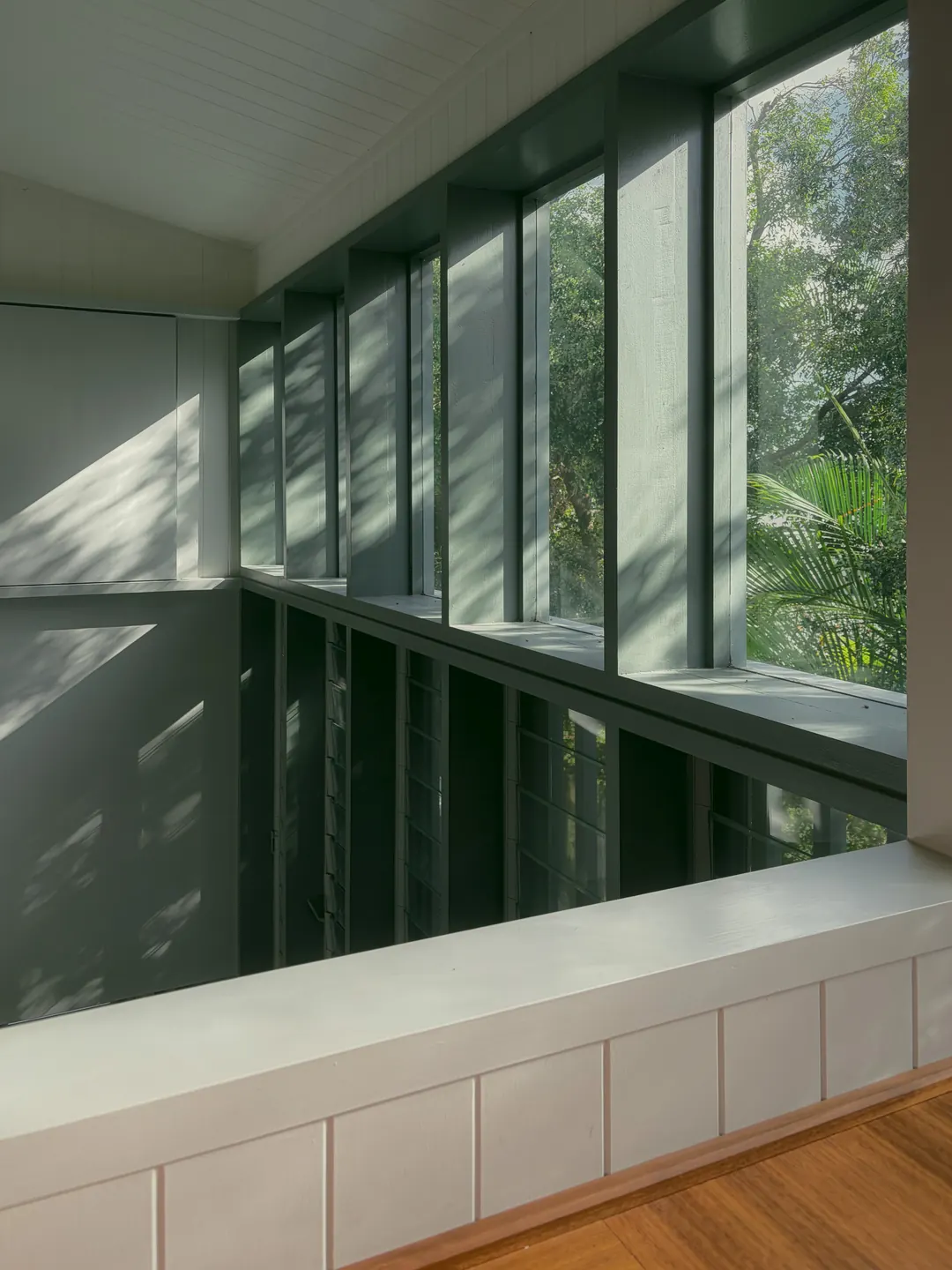 Dappled light on white VJ walls beside tall windows over the stair, upstairs in the Queenslander